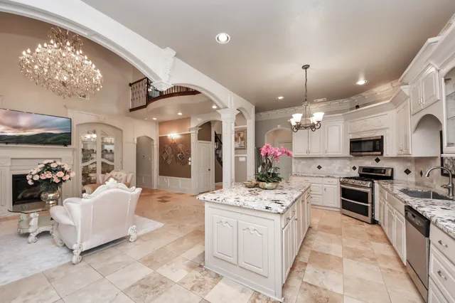 a large white kitchen with stainless steel appliances kitchen island granite countertop a sink dishwasher a stove a dining table and chairs with the kitchen view