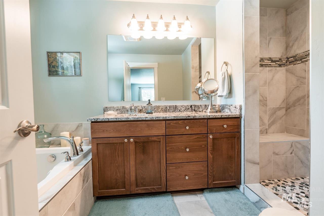 21 Melonie Loop Cascade, ID 83611 - Photo 16 of 27 Bathroom featuring a wood-finish vanity with a stone countertop, a large framed mirror, and a tiled shower with a mosaic accent band and built-in bench