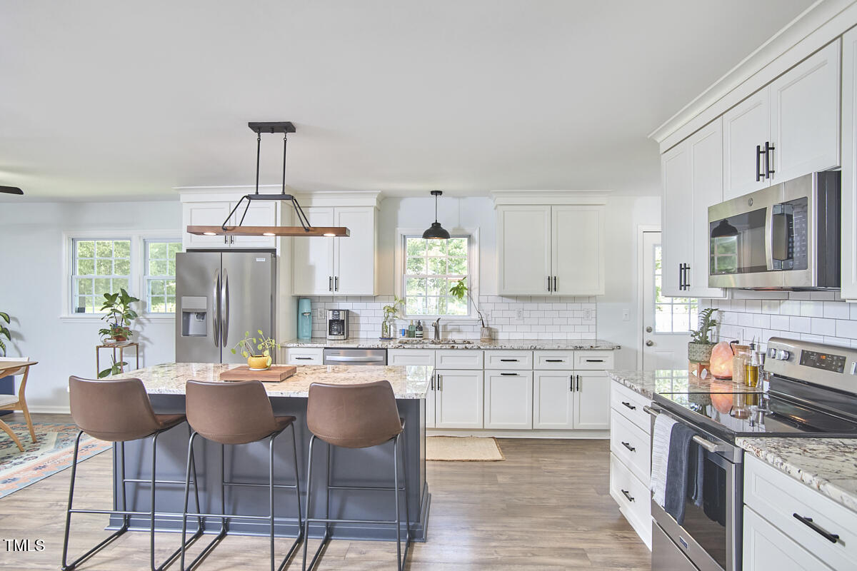 4103 Cheek Road Durham, NC 27704 - Photo 11 of 34 a kitchen with stainless steel appliances a dining table chairs stove and white cabinets