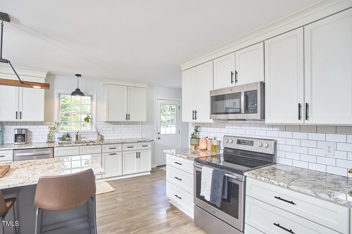 4103 Cheek Road Durham, NC 27704 - Photo 13 of 34 a kitchen with stainless steel appliances granite countertop a stove top oven a sink dishwasher and white cabinets with wooden floor