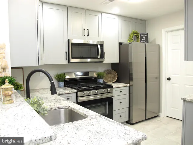 a kitchen with stainless steel appliances granite countertop a refrigerator a stove a sink and a white cabinets