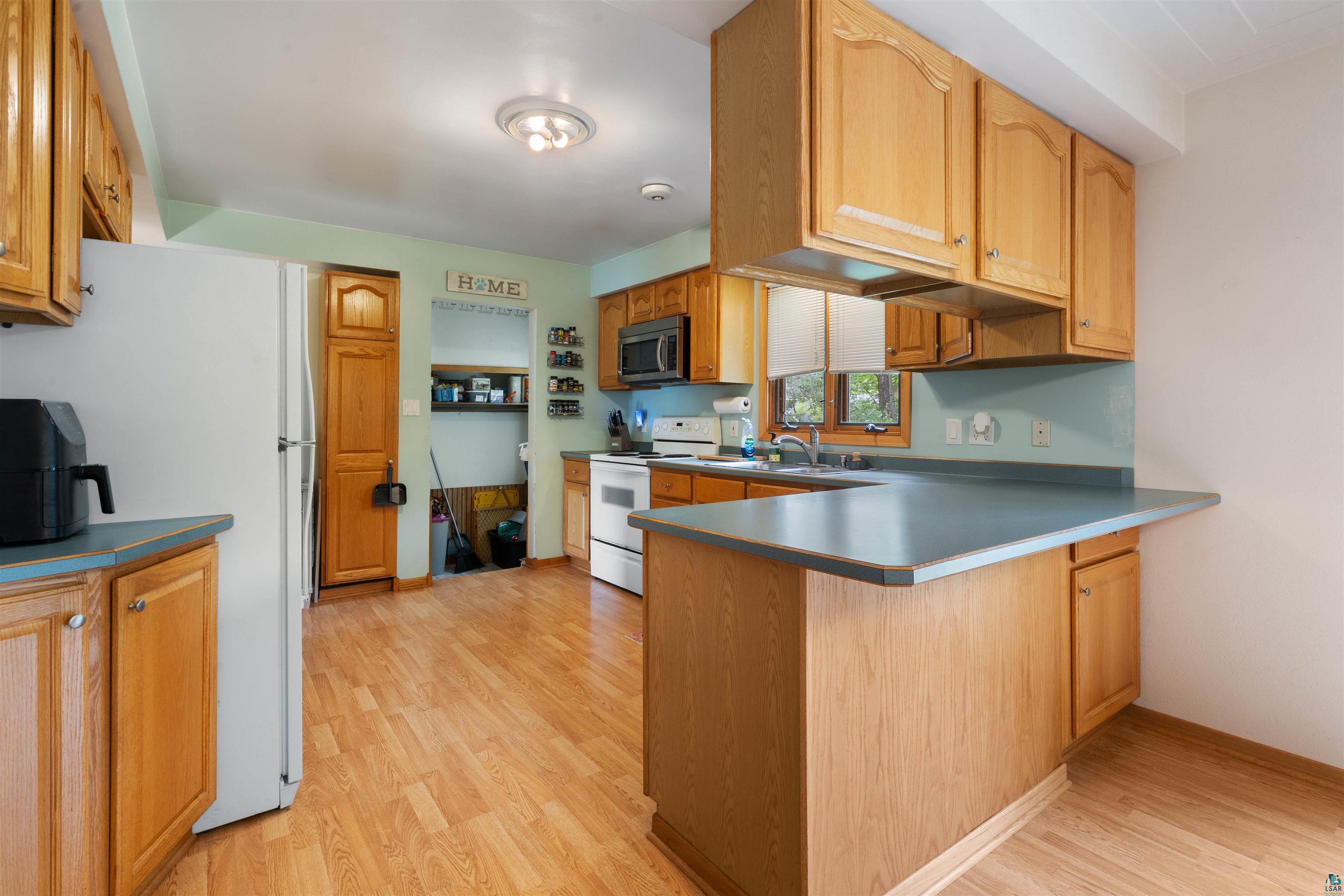 3711 Getchell Road Hermantown, MN 55811 - Photo 9 of 31 Kitchen featuring wood-finish flooring, light wood cabinetry, white appliances, and a built-in breakfast bar with a gray countertop