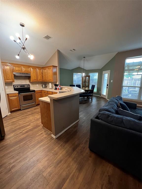 12201 Rolling Ridge Drive Fort Worth, TX 76028 - Photo 9 of 21 Open-concept living area featuring wood-finish flooring, a kitchen with wood cabinetry, stainless steel appliances, and a breakfast bar