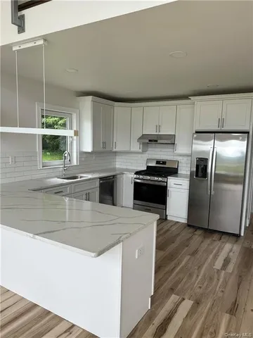 a kitchen with stainless steel appliances granite countertop a refrigerator a stove and a sink with wooden floor