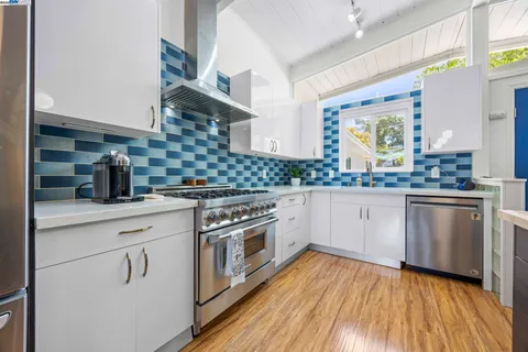 a kitchen with stainless steel appliances granite countertop wooden floor sink stove and white cabinets