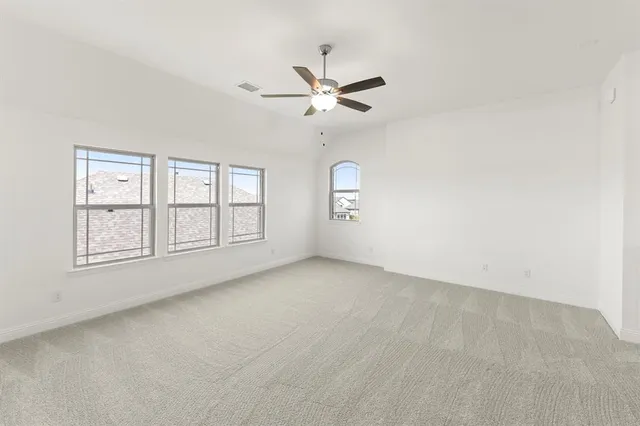 an empty room with chandelier fan and windows
