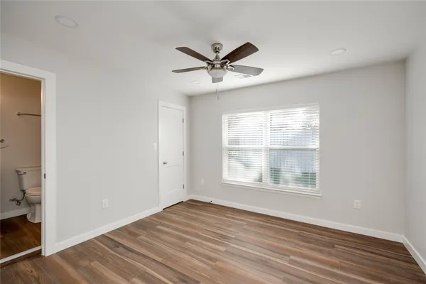 an empty room with wooden floor windows and fan