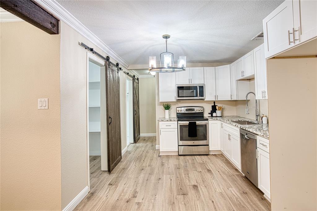 420 North Road Kennedale, TX 76060 - Photo 15 of 36 Kitchen with a barn door, stainless steel appliances, white cabinets, light wood-type flooring, and a chandelier