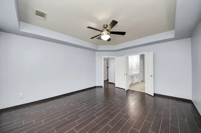 a view of an empty room with wooden floor and a ceiling fan