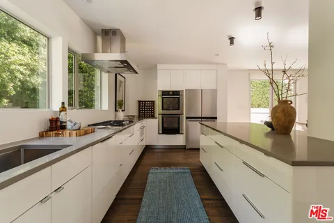 a large white kitchen with granite countertop a large window and stainless steel appliances