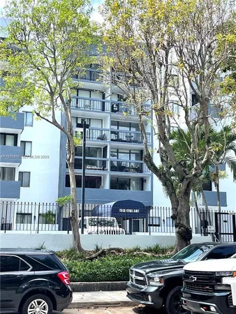 a front view of a building with lot of cars and trees