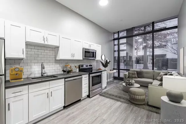 a kitchen with stainless steel appliances granite countertop a stove a sink dishwasher a microwave oven and a dining table with wooden floor