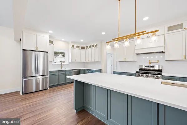 a large kitchen with kitchen island a stove a sink dishwasher a refrigerator and white cabinets with wooden floor