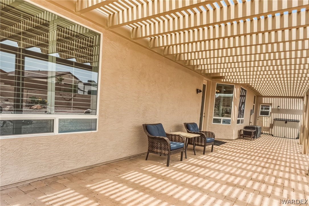 2708 Discovery Road Bullhead City, AZ 86442 - Photo 58 of 90 The property features a covered patio with an open lattice pergola, providing shade and a distinctive pattern of sunlight on the paver-tiled floor