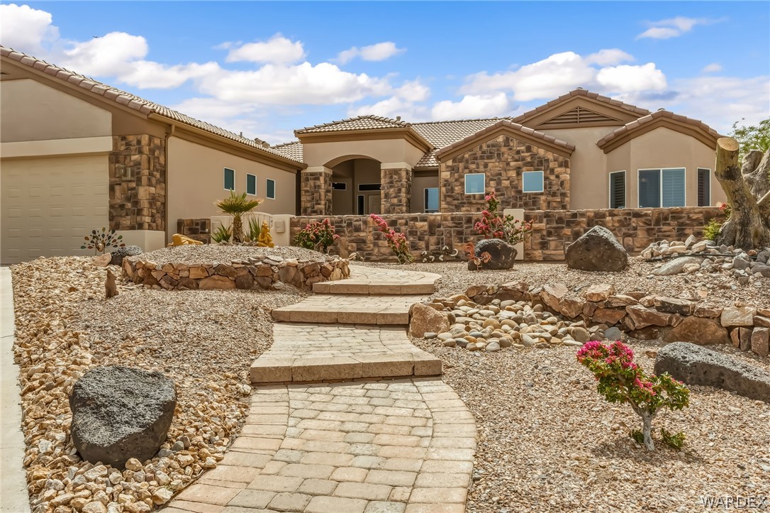2708 Discovery Road Bullhead City, AZ 86442 - Photo 6 of 90 The property features a desert-style landscaped front yard with a paved walkway, various rock formations, and low-maintenance plantings