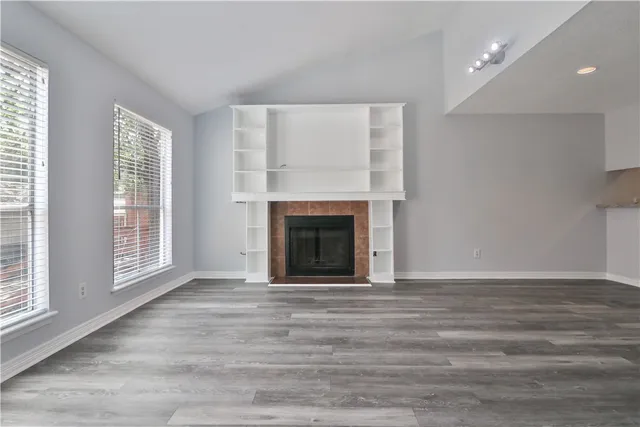 an empty room with wooden floor fireplace and windows