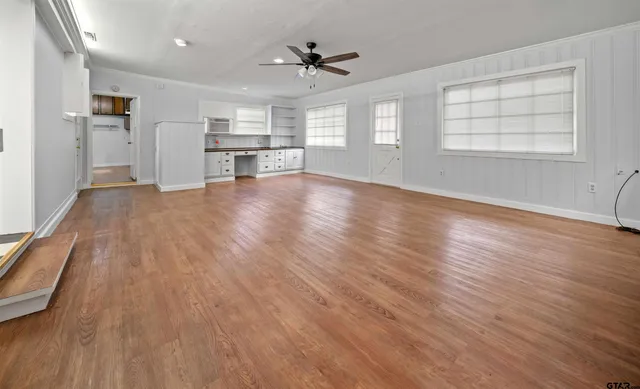 an empty room with wooden floor a ceiling fan and windows