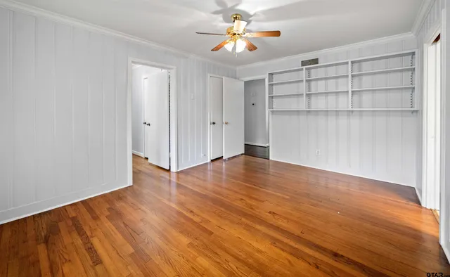 a view of empty room with wooden floor and fan