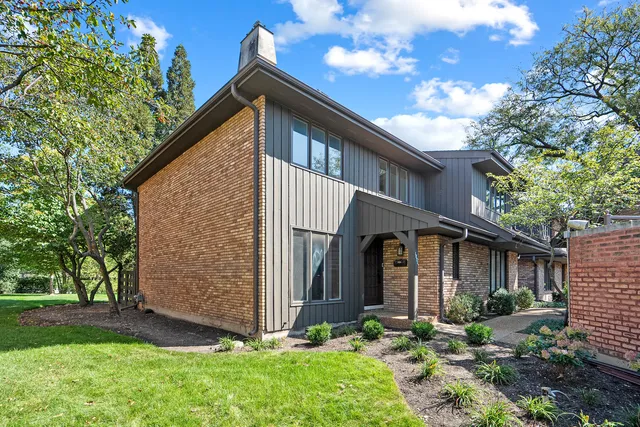 a view of a house with brick walls plants and large tree