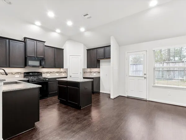 a kitchen with stainless steel appliances granite countertop wooden cabinets a refrigerator a stove a sink and a oven with wooden floors