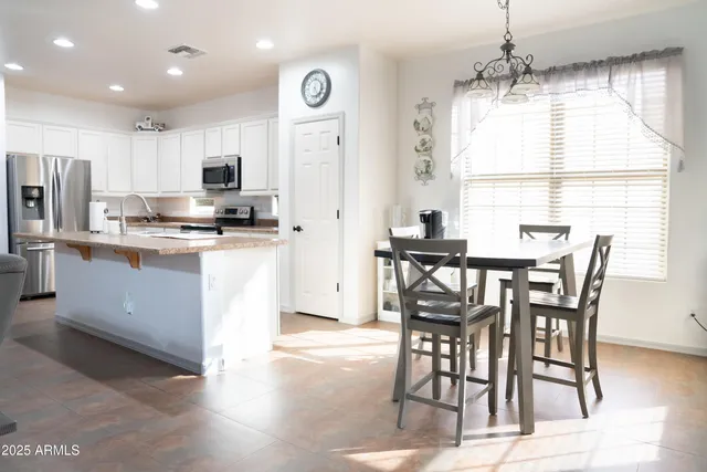 a kitchen with stainless steel appliances kitchen island granite countertop a stove a refrigerator a sink a dining table and chairs with wooden floor