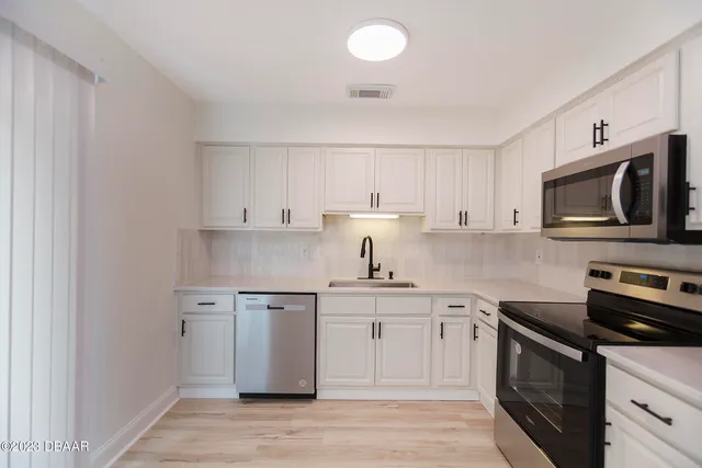 a kitchen with stainless steel appliances granite countertop a sink a stove top oven and white cabinets