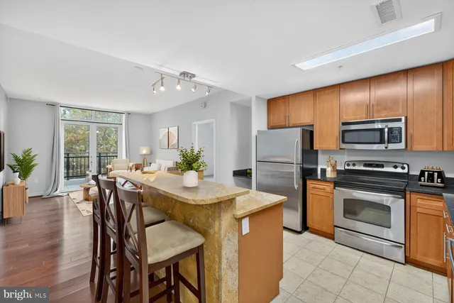 a kitchen with stainless steel appliances granite countertop a stove a refrigerator a kitchen island a stove a dining table and chairs with wooden floor