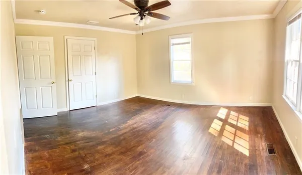 an empty room with wooden floor fan and windows