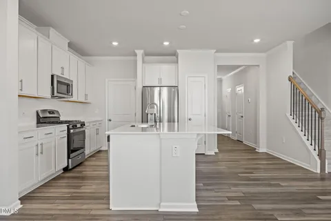 a large kitchen with stainless steel appliances granite countertop a stove top oven a refrigerator a sink and white cabinets with wooden floor