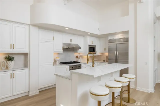 a kitchen with stainless steel appliances kitchen island granite countertop a sink a stove a refrigerator and white cabinets with wooden floor