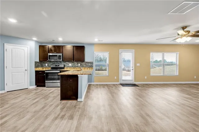 a kitchen with stainless steel appliances granite countertop a stove top oven a sink dishwasher a microwave oven and a refrigerator with wooden floor