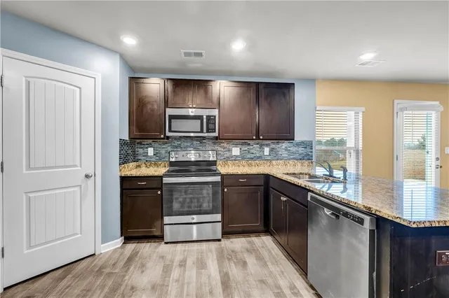 a large kitchen with granite countertop a stove top oven a sink dishwasher a refrigerator and cabinets with wooden floor