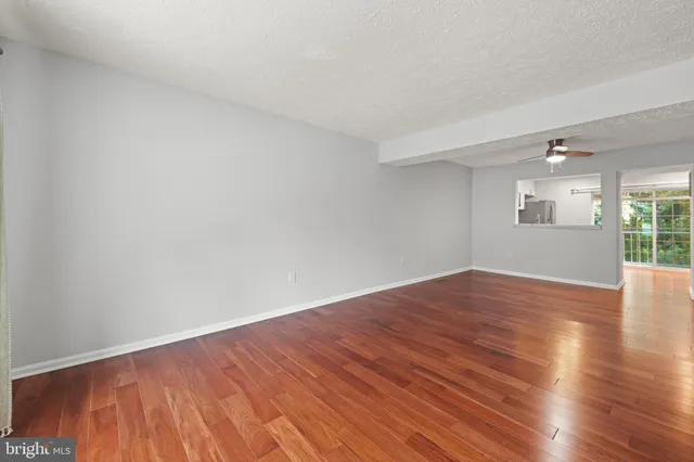 a view of empty room with wooden floor and fan