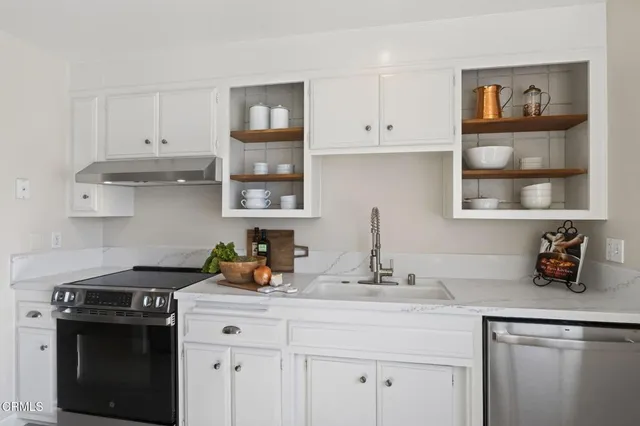 a kitchen with stainless steel appliances a stove a sink and white cabinets with wooden floor