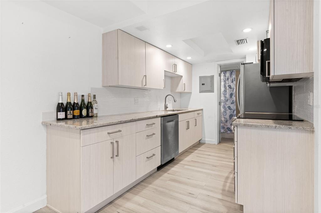 8921 Blind Pass Road, Unit 142 St. Pete Beach, FL 33706 - Photo 13 of 22 a kitchen with stainless steel appliances granite countertop a sink dishwasher a refrigerator and white cabinets with wooden floor