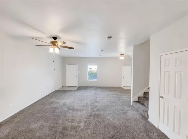 an empty room with chandelier fan and windows