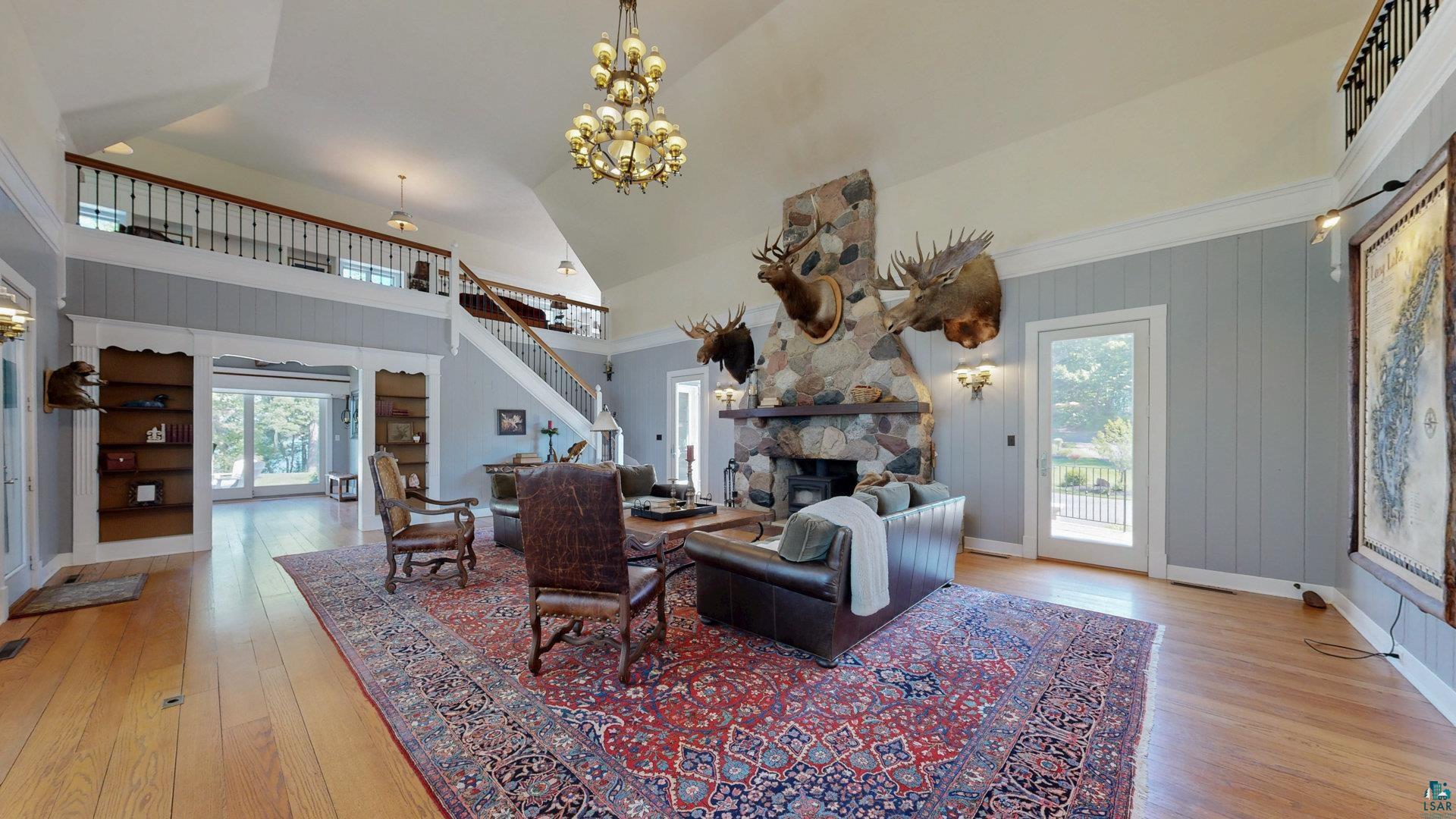 N1211 East Side Road Birchwood, WI 54817 - Photo 14 of 70 Living area featuring a fireplace, light wood-type flooring, stairway, high vaulted ceiling, and a chandelier
