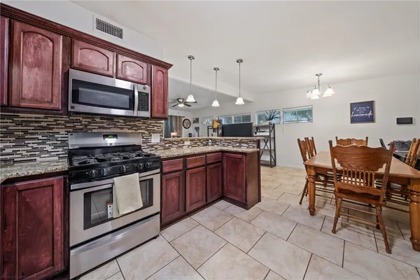 a kitchen with stainless steel appliances granite countertop a stove top oven a sink dishwasher a dining table and chairs with wooden cabinets