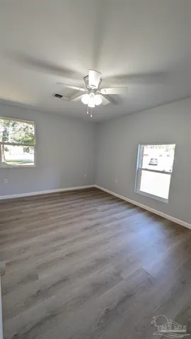 an empty room with wooden floor chandelier fan and windows