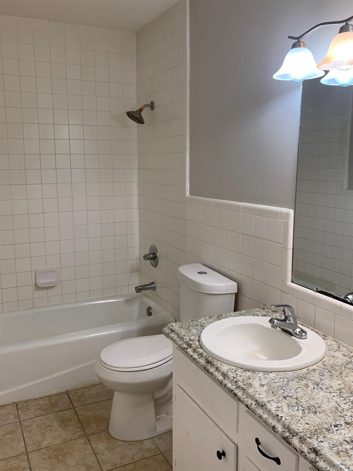 4316 58th Street, Unit A Lubbock, TX 79413 - Photo 9 of 10 a bathroom with a granite countertop toilet a sink and bathtub