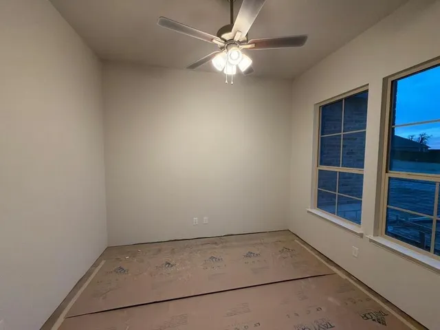 an empty room with a chandelier fan and windows