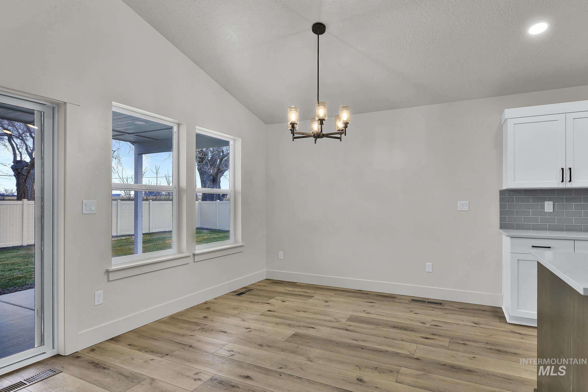 1130 Velvet Loop Wilder, ID 83676 - Photo 10 of 35 Dining area with vaulted ceilings, wood-finish flooring, and a contemporary chandelier