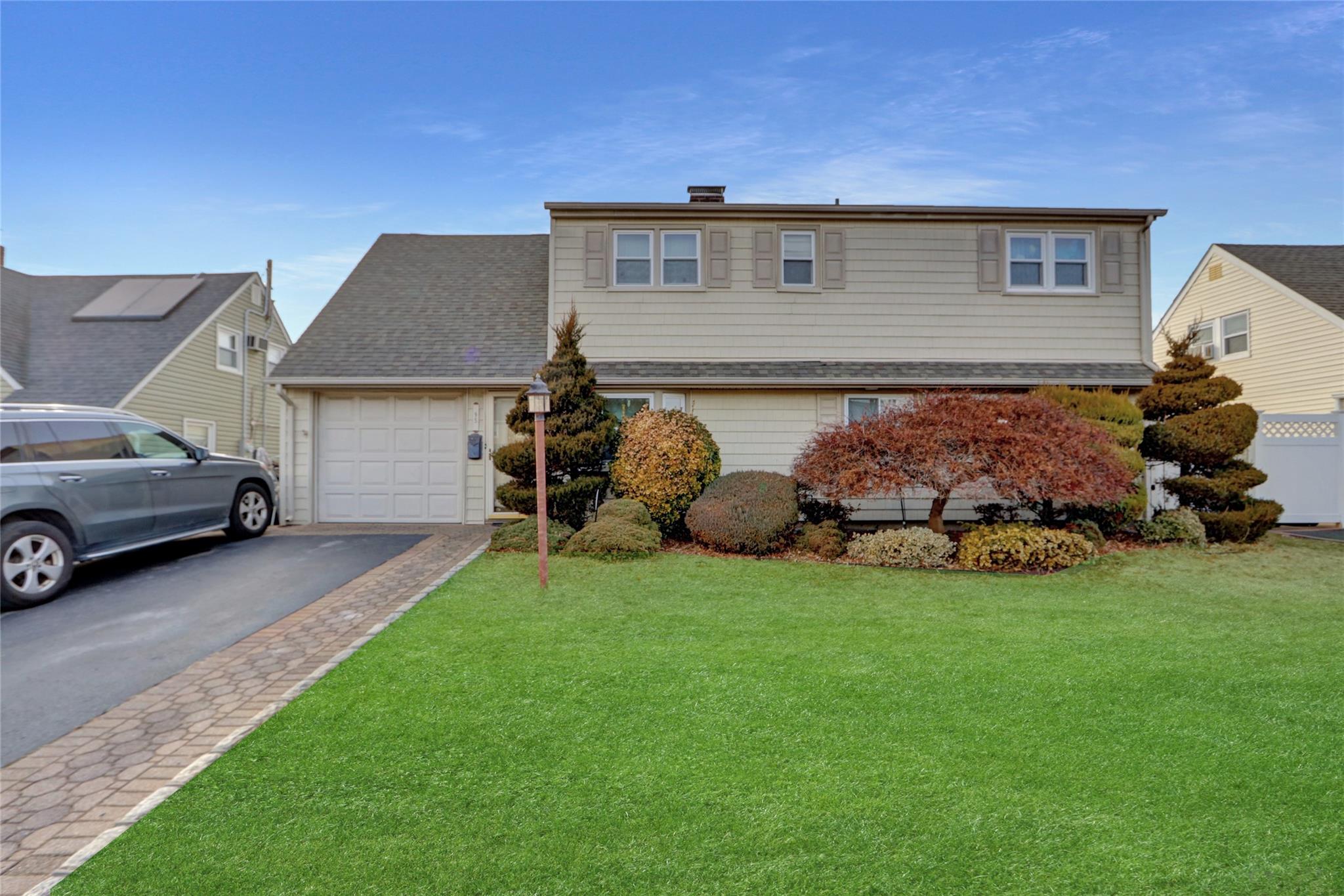 Traditional home with a garage, roof with shingles, driveway, and a front lawn