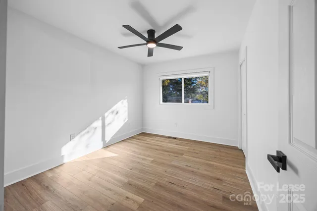 a view of an empty room with wooden floor and a ceiling fan