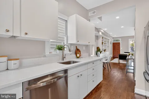 a kitchen with a sink dishwasher stove and white cabinets with wooden floor