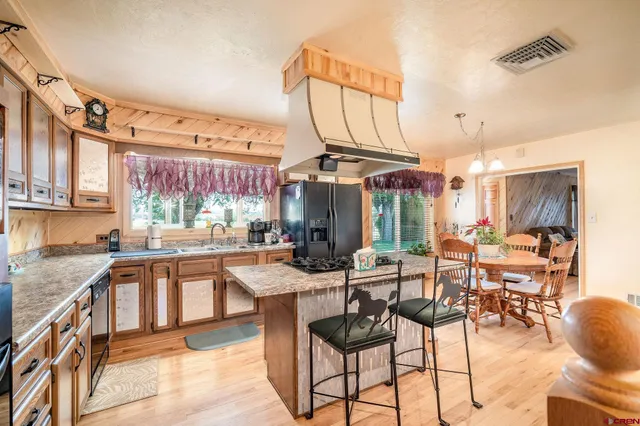 a kitchen with stainless steel appliances kitchen island granite countertop a stove a sink dishwasher and a refrigerator with wooden floor