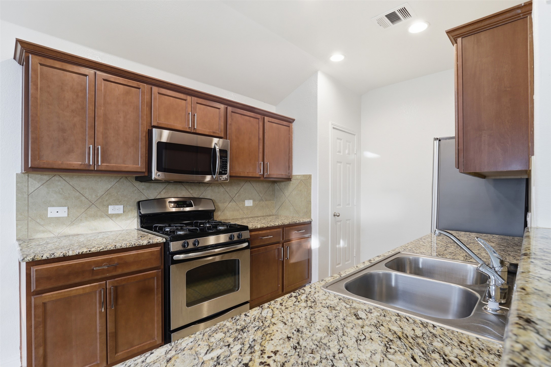 448 Nottingham Loop Kyle, TX 78640 - Photo 3 of 16 Kitchen featuring granite countertops, wood cabinetry, stainless steel gas range, stainless steel microwave, and dual basin sink