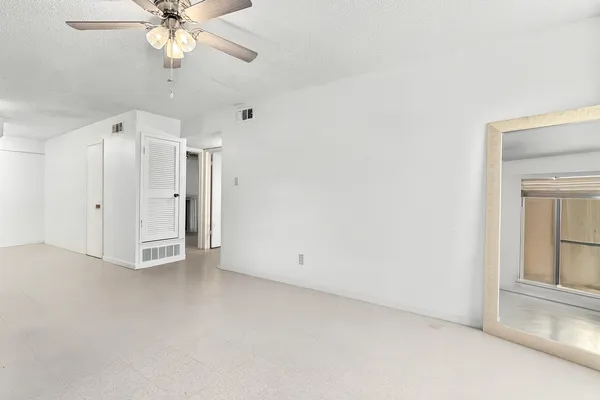 an empty room with chandelier fan and windows