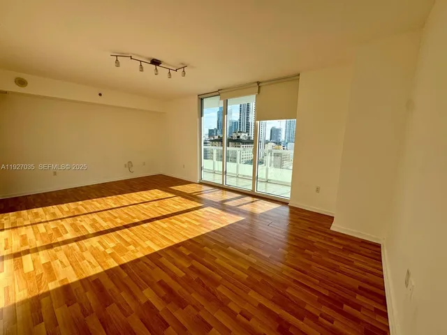 a view of an empty room with wooden floor and a window