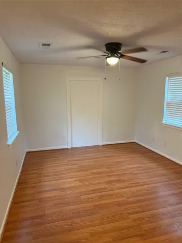 a view of an empty room with wooden floor and fan